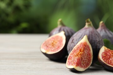 Whole and cut ripe figs on light wooden table against blurred green background, closeup. Space for text