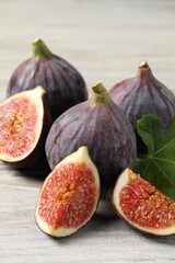 Whole and cut ripe figs on light wooden table, closeup