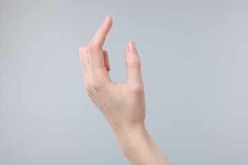 Woman holding something in fingers on grey background, closeup