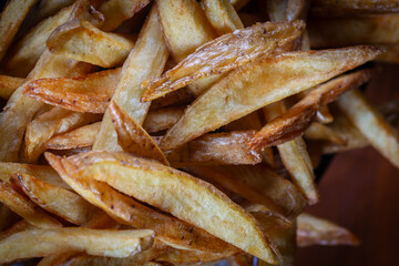 French fries served on a basket, cutting board on a black wooden table. Rustic french fries, hand made.