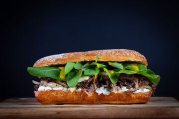 Shredded beef sandwich with arugula and caramelized onion, mustard sauce on wooden table. Delicious lunch