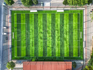 Aerial bird-eye view of a Mini Soccer court with stripped green color and trees. Young people are...