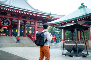 Back view full body of unrecognizable Hispanic tourist backpacker standing on street tiled pavement against entrance of Japanese Sensoji temple in Asakusa Tokyo, Japan - obrazy, fototapety, plakaty