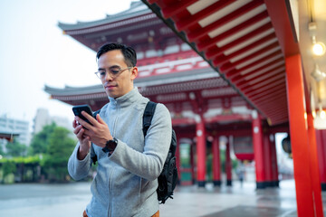 Hispanic tourist guy standing on blurred background of Japanese temple Sensoji  and sending text...