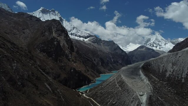 Camera slowly moving around a hill to reveal Laguna Paron with pale blue water and snowcapped peaks in the background cloudy day