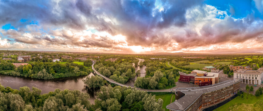 Aerial panoramic view of Living Bridge, curving modern pedestrian crossing over the Shannon river at the University of Limerick with stunning sunset