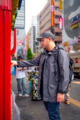 Side view of concentrated young Hispanic male tourist in warm clothes and cap with backpack taking photo on buildings on smartphone while standing in Akihabara neighborhood in Tokyo, Japan