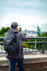 Unrecognizable young Hispanic male tourist in jacket and cap with backpack taking photos with...
