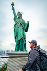 Side view of serious young Hispanic male tourist in jacket and cap with backpack standing near...