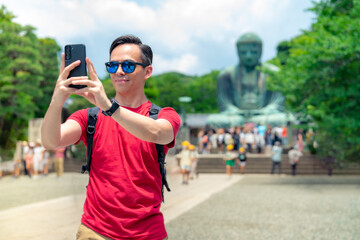 Happy young Hispanic male in casual red t-shirt with sunglasses and backpack taking selfie on...