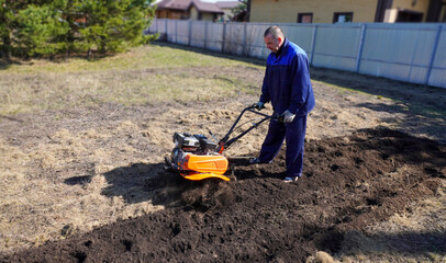 A man works in a vegetable garden in early spring. Digs the ground.  Works as a cultivator, walk-behind tractor.