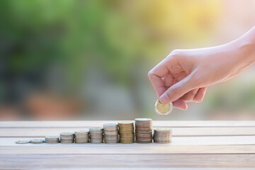 business woman hand holding coin with stack of money coins on wood table