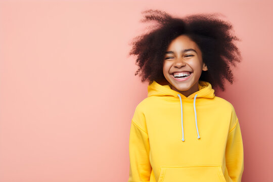 Colourful portrait of a young black happy girl laughing and smiling wearing yellow hoody on bright pink background