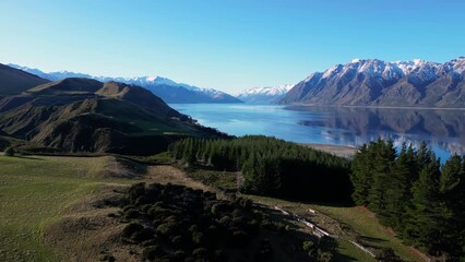 Hawea, New Zealand: Dramatic aerial drone footage of the coastal raod along lake Hawea in Wanaka on a sunny winter in New Zealand south island. - Powered by Adobe