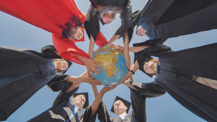 College graduates join hands over a globe of the world overlooking Africa. The concept of world...