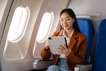 using tablet pc, Elegantly dressed brown suit Asian chinese japanese people businesswoman immersed in work, comfortably seated onboard, capturing the merging worlds of corporate hustle - obrazy, fototapety, plakaty