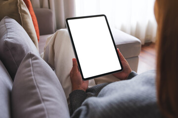 Mockup image of a woman holding digital tablet with blank desktop screen while lying on a sofa at...