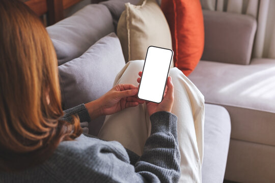 Mockup image of a woman holding mobile phone with blank desktop white screen while lying on a sofa at home