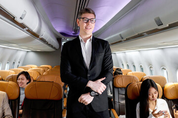 Portrait of happy smiling businessman in black suit, standing on aisle inside airplane, male passenger traveling on business trip by aircraft, businesspeople traveling with airline transportation.