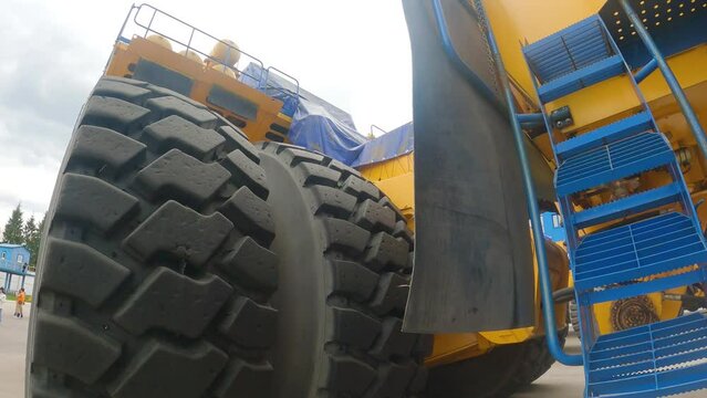 A girl passing under a large dump truck. Close-up of huge wheels of the truck, yellow frame and other elements of construction. Excursion at the factory of the manufacturer of quarry equipment