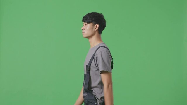 Side View Of Asian Man Worker Walking And Looking Around In The Green Screen Background Studio
