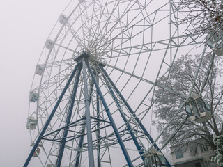 Ferris wheel in the winter park in winter during the appearance of fog. Fog in winter at the amusement park. Rides in the park in winter. Fog in the city park. Entertainment for vacationers.