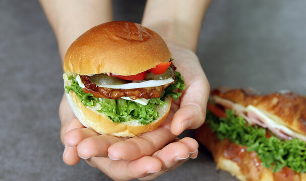 Close up image of a hand holding a hamburger. Bread with vegetables and meat patties.
