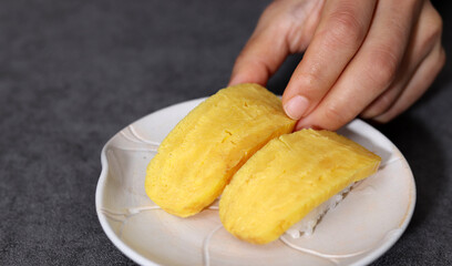 Close-up images of healthy and fresh sushi. Close-up image of picking up egg sushi with fingers.
