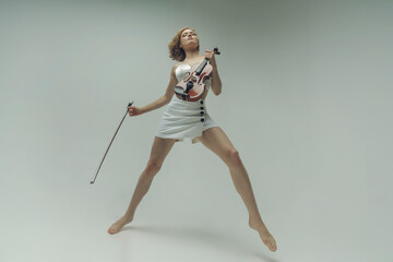 young blonde female musician plays the violin moving on one leg