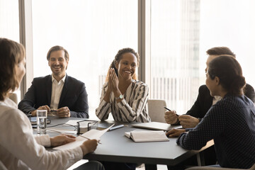 Cheerful young diverse office friends working on business project together, discussing common tasks, planning successful strategy, talking at meeting table, laughing, relaxing
