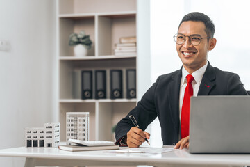 Agent presents contracts for property purchase or lease. Businessman asian indian people showcases miniature model home, signifying secure property insurance. Desk scene in a home sales office.