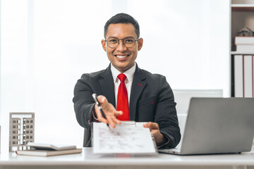 Agent presents contracts for property purchase or lease. Businessman asian indian people showcases miniature model home, signifying secure property insurance. Desk scene in a home sales office.