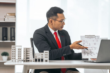 Fototapeta na wymiar Agent presents contracts for property purchase or lease. Businessman asian indian people showcases miniature model home, signifying secure property insurance. Desk scene in a home sales office.