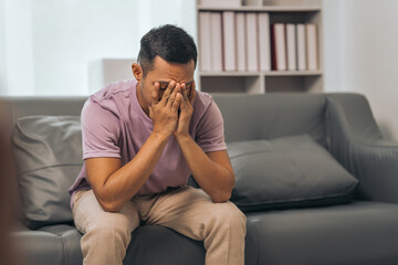 Middle-aged Asian Indian man with psychosis, depression, headache, migraine, sitting on sofa.