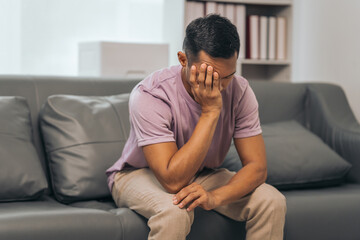 Middle-aged Asian Indian man with psychosis, depression, headache, migraine, sitting on sofa.