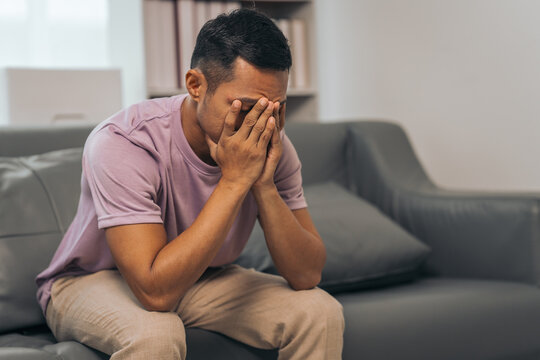Middle-aged Asian Indian man with psychosis, depression, headache, migraine, sitting on sofa.