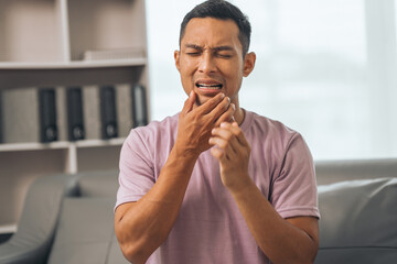 Middle-aged Asian Indian man with gum disease, toothache, wisdom tooth and molar pain. sitting on the sofa