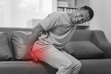 Middle-aged Asian Indian man with butt pain, hemorrhoids, colon pain, sitting on a sofa.