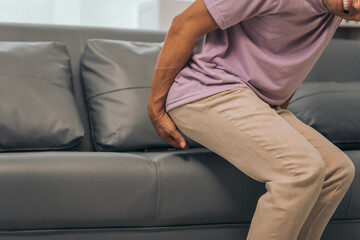 Middle-aged Asian Indian man with butt pain, hemorrhoids, colon pain, sitting on a sofa.
