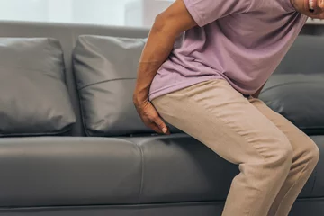Foto op Canvas Middle-aged Asian Indian man with butt pain, hemorrhoids, colon pain, sitting on a sofa. © NanSan