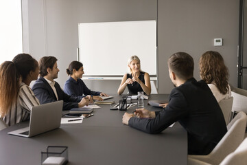 Confident middle aged team leader woman meeting with diverse group in boardroom, talking to employees, discussing work tasks, plan, strategy. Corporate teacher giving seminar to staff - obrazy, fototapety, plakaty