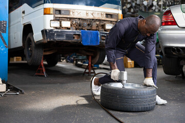 Fototapeta na wymiar African mechanic worker fixing tire with old car in garage