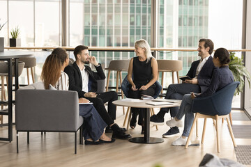 Happy diverse business team sitting in circle in modern office lobby interior, contemporary co-working space, discussing teamwork strategy, cooperation, smiling, laughing, enjoying conversation