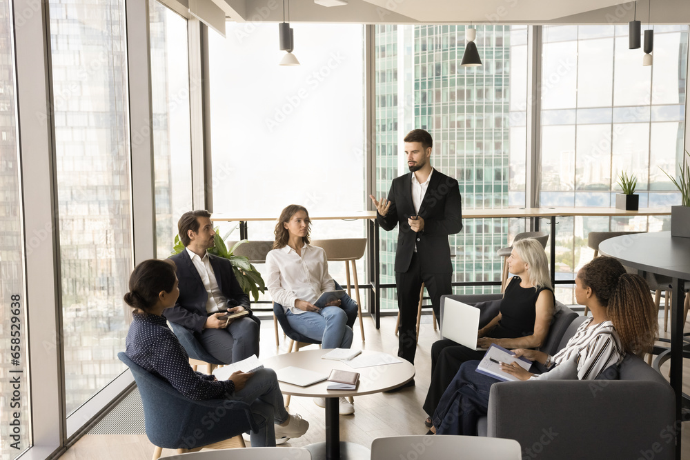 Poster Confident young business leader man talking to diverse group on meeting. Male chief, project manager meeting with employees, discussing project plan, teamwork strategy, tasks