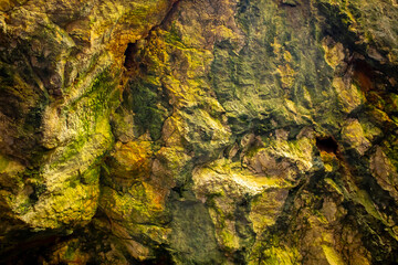 Natural rock texture background. Rocky bas-relief wall. Green moss on the surface of the rocks.