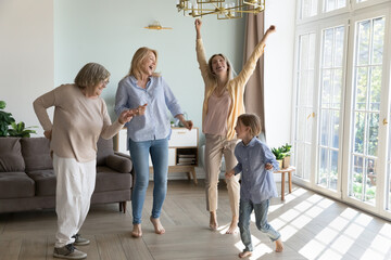 Happy cheerful girls and women of four female generations enjoying family party, energetic activity, dancing at home in living room, singing, laughing, celebrating mothers day