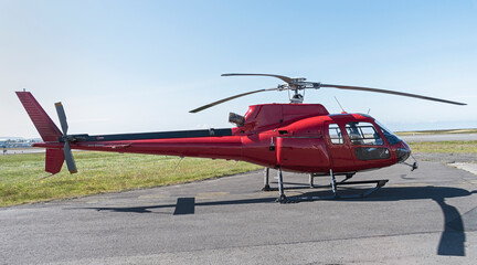 small red tourist helicopter sitting on the ground at an airport with a clear blue sky in the background and tarmac in the foreground