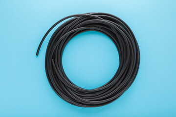 Black dark rolled cable on light blue table background. Pastel color. Closeup. Top down view.