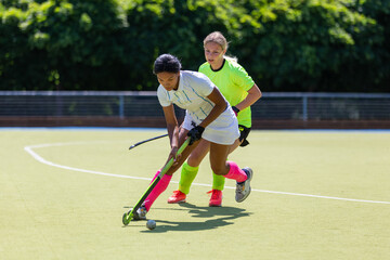 Two female field hockey players fighting for the ball on the pitch in attack