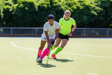 Two female field hockey players fighting for the ball on the pitch in attack